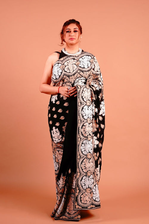 A woman standing in a pose wearing a black and gold Kashmiri embroidered saree with floral patterns.
