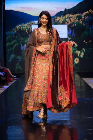 Model wearing a traditional outfit with a vibrant design on a stage with a scenic background