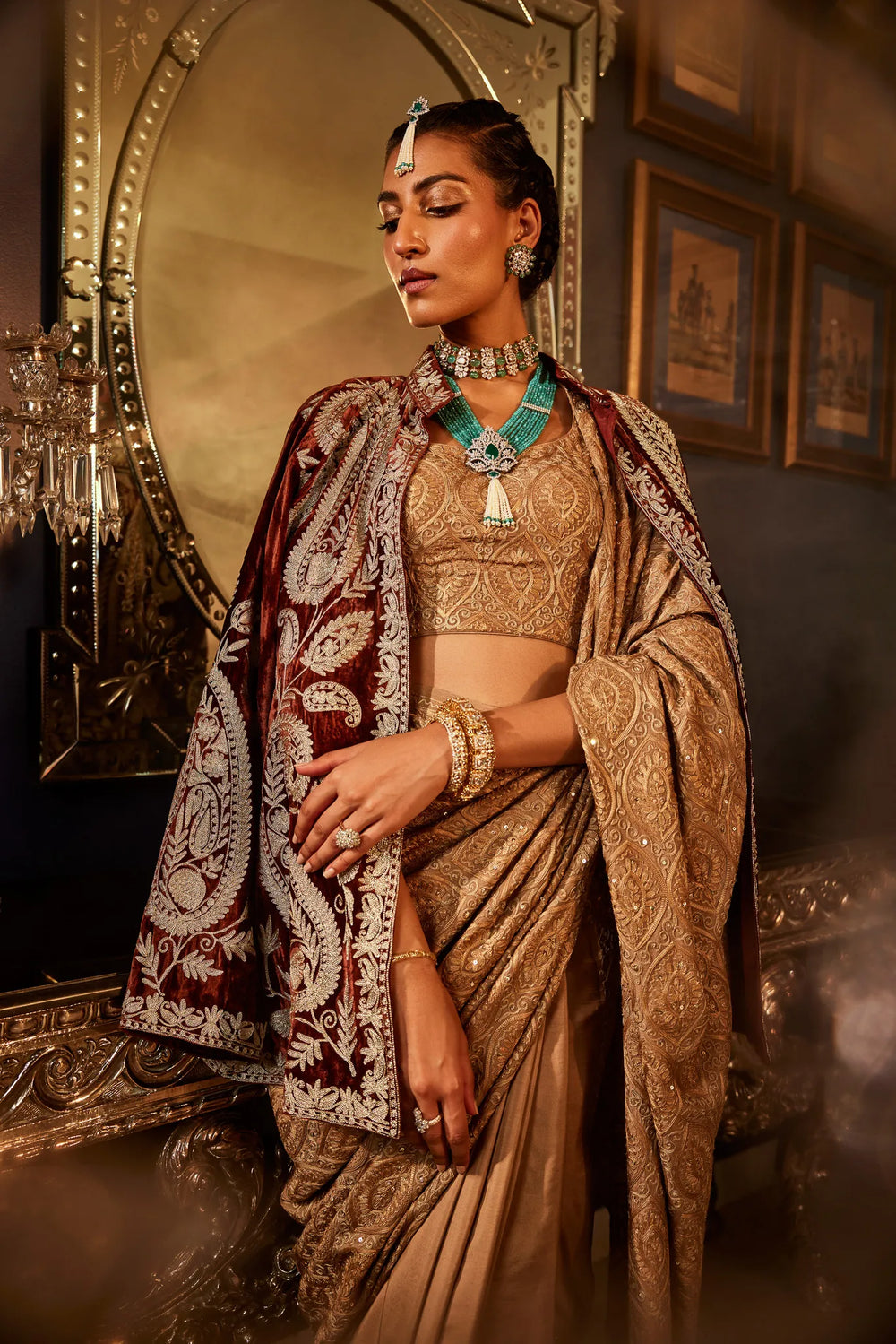 A woman draped in a brown saree with golden and silver sequence work, standing in a luxurious interior setting.