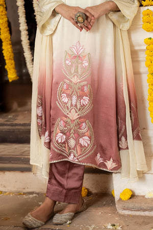 #OmbreCream&Mauve Traditional outfit with intricate embroidery, held by a person, against a decorated background.