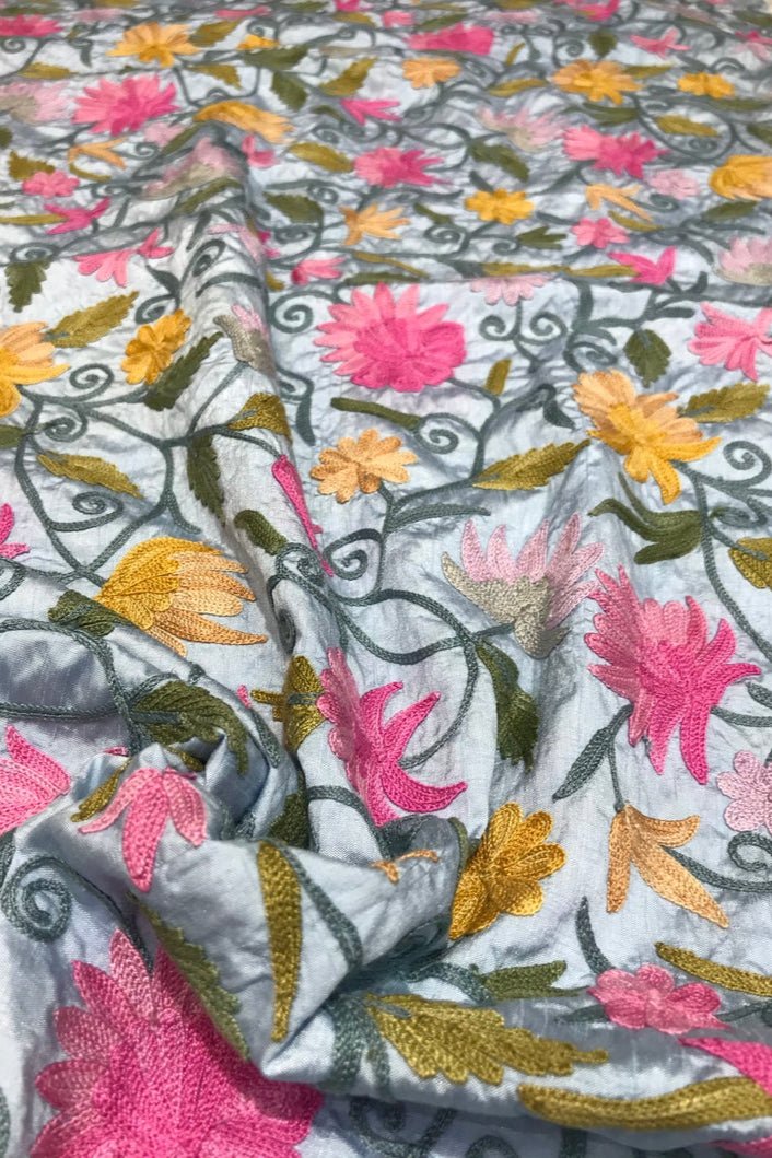 Embroidered fabric with floral patterns in pink, yellow, and green on a blue background
