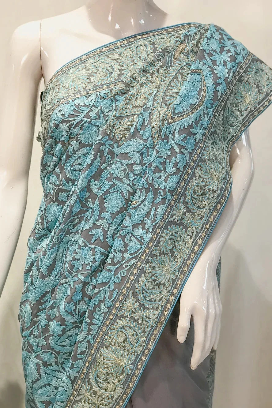 #LightGrey Mannequin wearing a blue and gray saree with a small table and floral arrangement in the background.