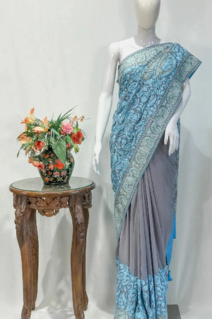 #LightGrey Mannequin wearing a blue and gray saree with a small table and floral arrangement in the background.
