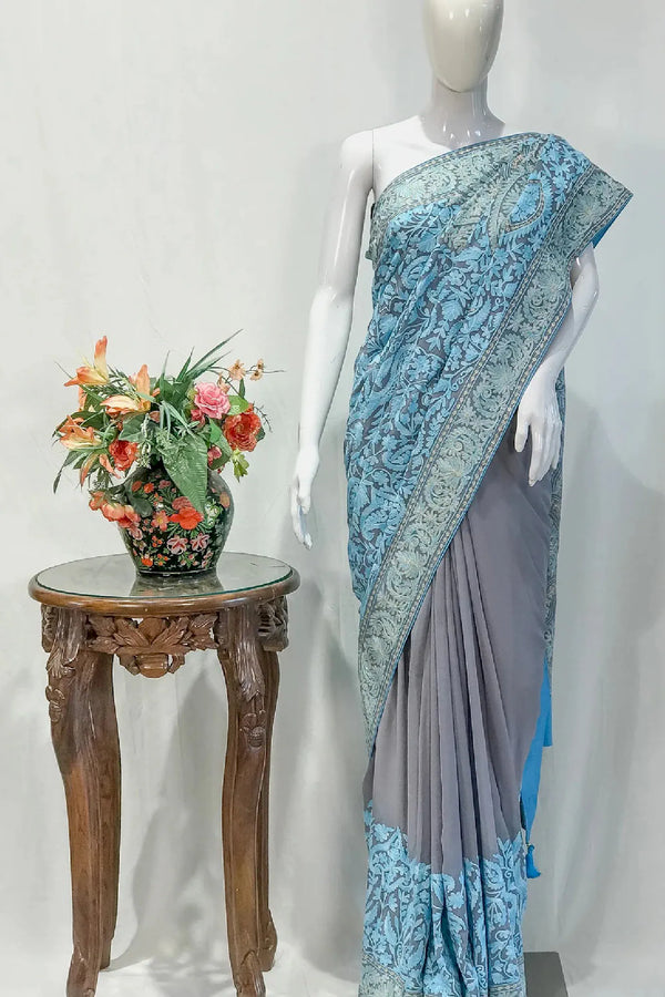 #LightGrey Mannequin wearing a blue and gray saree with a small table and floral arrangement in the background.