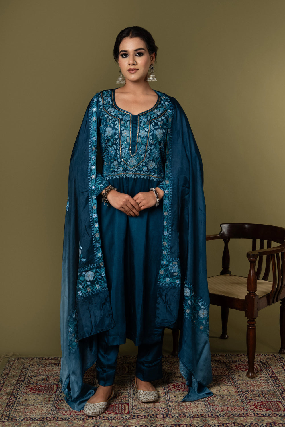 #TealBlue Woman wearing a blue embroidered traditional outfit standing against a plain background
