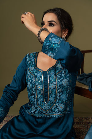 #TealBlue Woman wearing a blue embroidered traditional outfit with a plain background