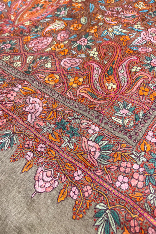 Close-up of a patterned fabric with intricate designs in pink, orange, and green on a beige background.