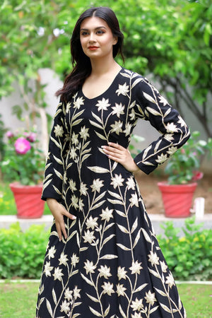 Woman wearing a black dress with white floral patterns standing outdoors.