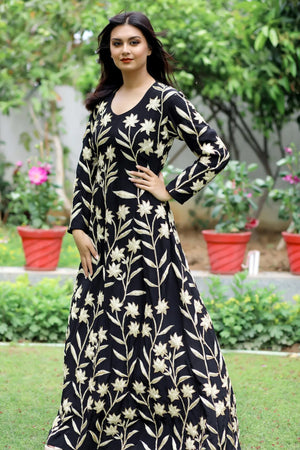 Woman wearing a black floral dress standing outdoors with greenery in the background
