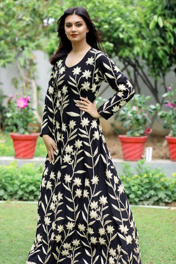 Woman wearing a black floral dress standing outdoors with greenery in the background