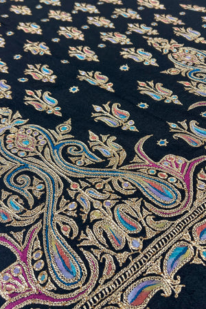 Close-up of intricate paisley pattern fabric with metallic threads on a dark background