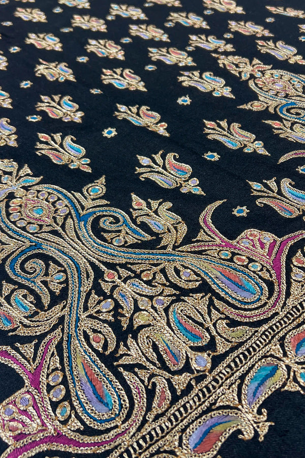 Close-up of intricate paisley pattern fabric with metallic threads on a dark background