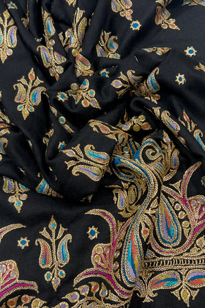 Close-up of black fabric with intricate gold, blue, and pink paisley patterns.