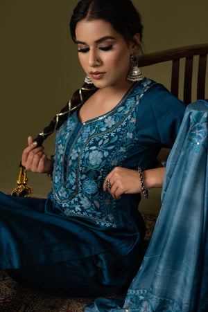 #TealBlue Woman in a blue embroidered traditional outfit sitting on a chair.