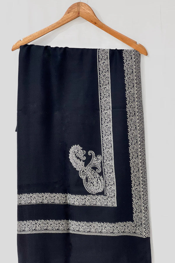 #Black - Black wool shawl with ivory machine-woven double border and paisley corner medallion, Kashmiri design, hanging flat on a wooden hanger