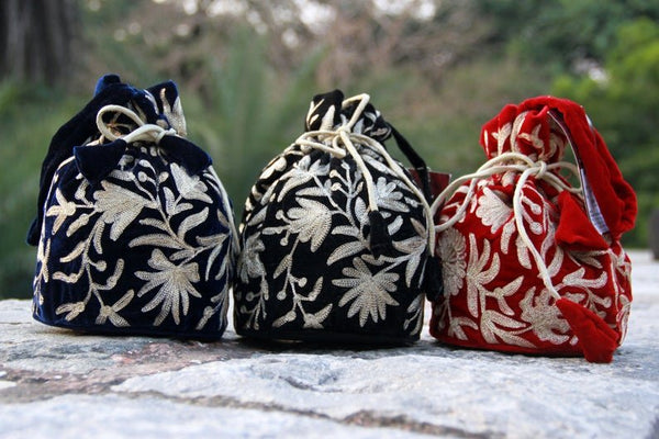 Three drawstring bags in black, navy, and red with floral patterns on a stone surface.