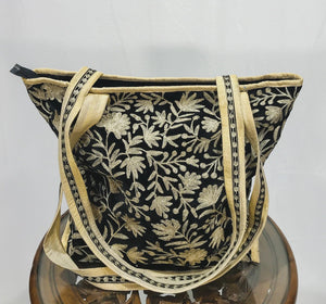 Black floral embroidered bag with gold trim on a white background