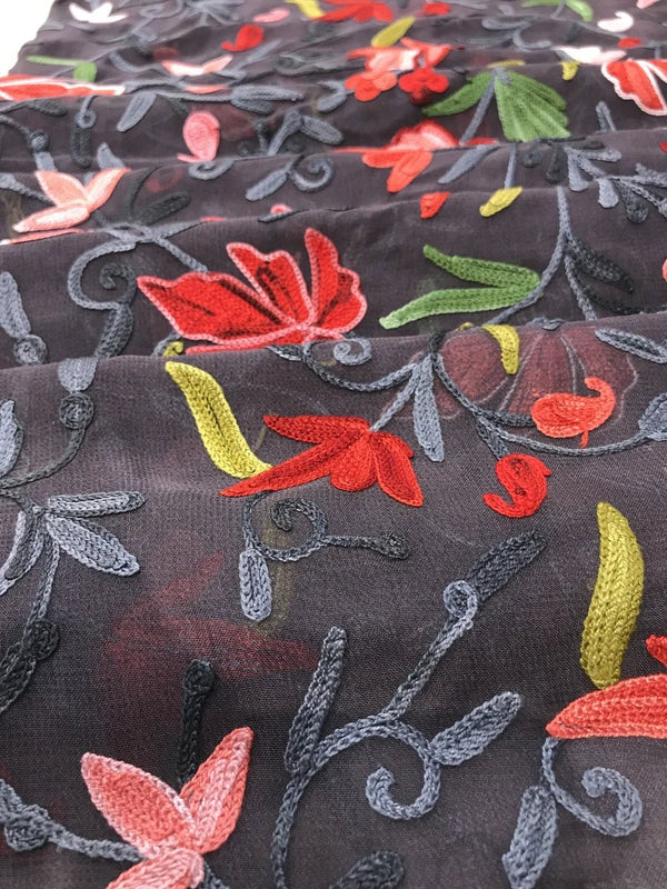Close-up of embroidered fabric with colorful floral patterns on a grey background