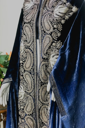 Blue velvet garment with intricate white embroidery on a neutral background