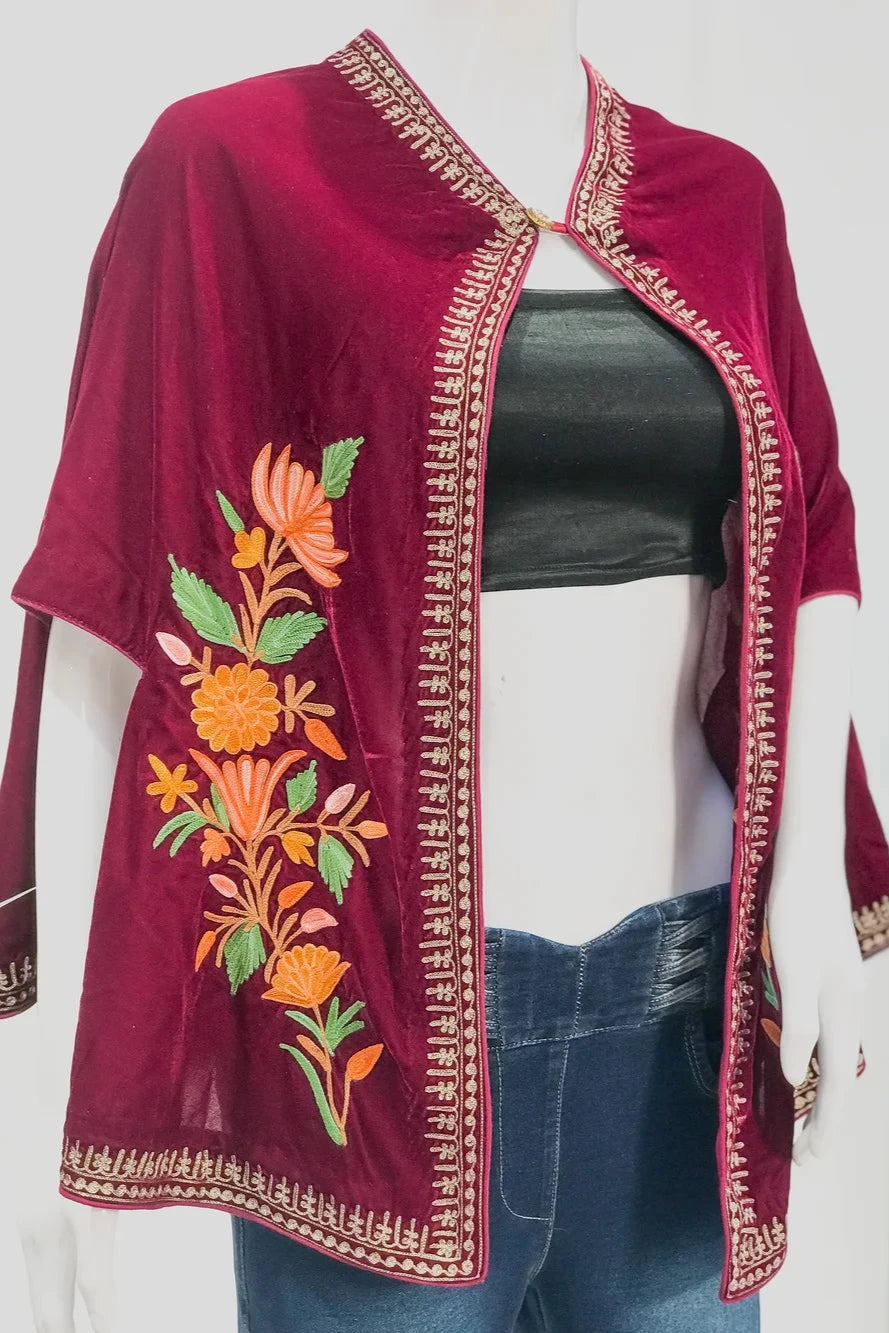 Mannequin wearing a burgundy embroidered top with floral patterns next to a small table with flowers on a white background