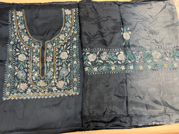 Two pieces of fabric, one with a floral Aari and sequence work in the center and the other with a border featuring the same style of work.