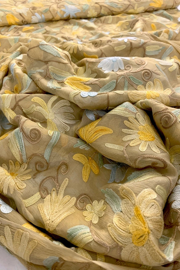 Beige Embroidered fabric with floral patterns in beige, yellow, and green on a white background