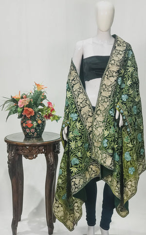 #Green Mannequin wearing a floral patterned green and gold cape with a small table and flowers in the background.