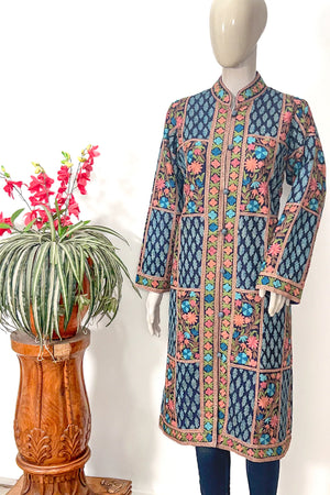 Colorful embroidered coat on a mannequin with a plant in the background