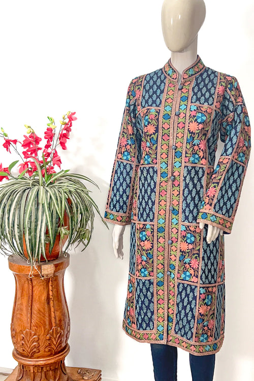 Colorful embroidered coat on a mannequin with a plant in the background