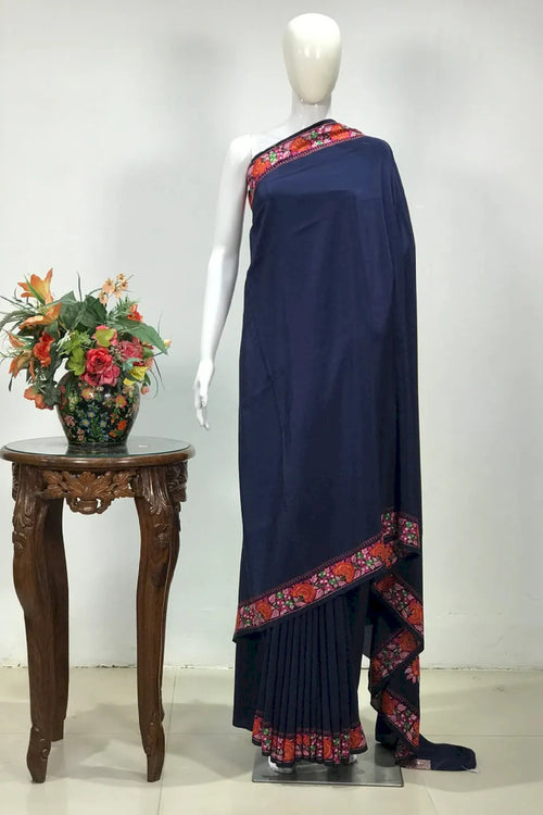 #Navyblue saree with floral border on a mannequin, next to a wooden table with flowers, against a white background.