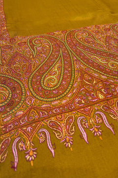 Close-up of a patterned fabric with intricate designs on a mustard yellow background