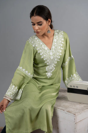 #MossGreen Woman wearing a green dress with white embroidery sitting on a wooden bench.