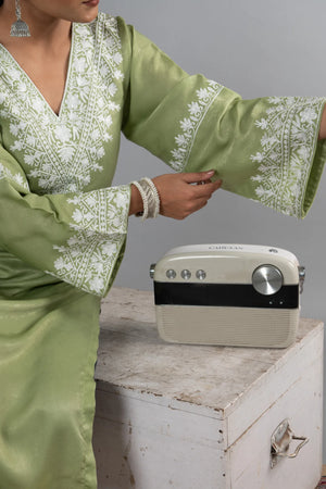 #MossGreen Person wearing a green embroidered outfit with a vintage radio on a wooden surface.