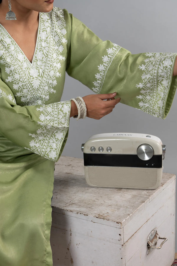 #MossGreen Person wearing a green embroidered outfit with a vintage radio on a wooden surface.