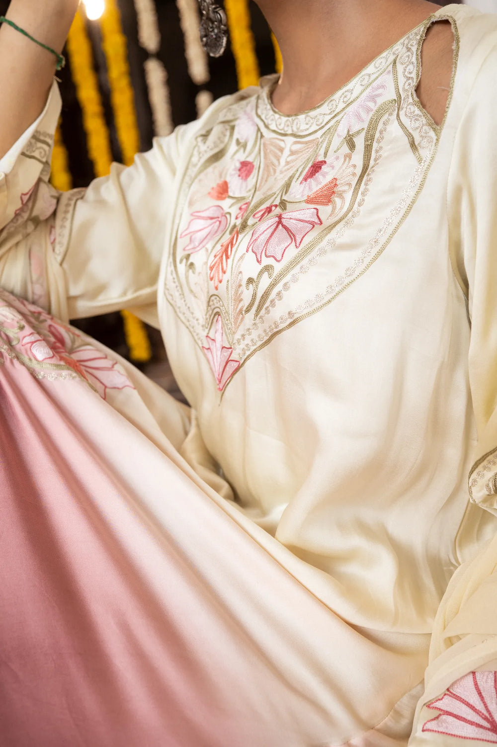#OmbreCream&Mauve Woman in traditional outfit standing in front of a decorated entrance with yellow flowers.