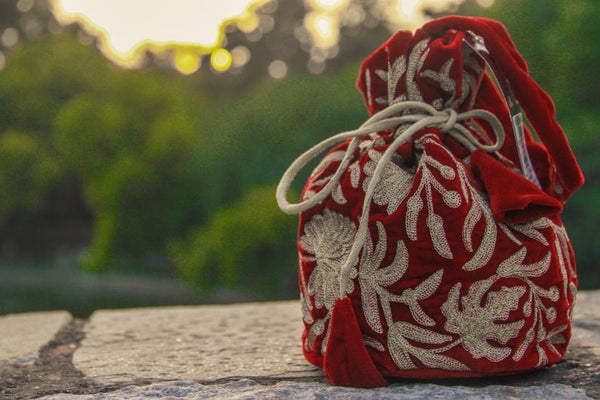 #Red Red fabric bag with white floral embroidery on a stone surface with a blurred natural background