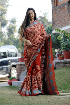 Woman in a red saree with patterns standing outdoors.