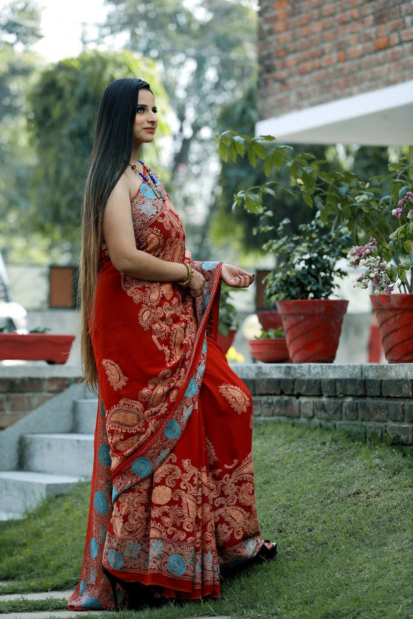 Woman in a red saree with floral patterns standing outdoors.