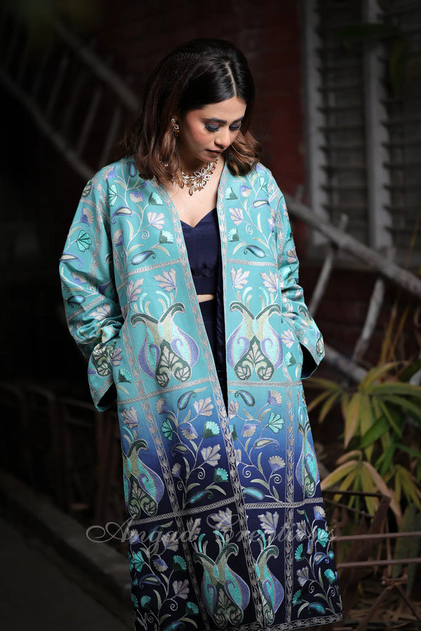 #OmbreBlue&Green Woman wearing a long, patterned turquoise jacket with a dark background