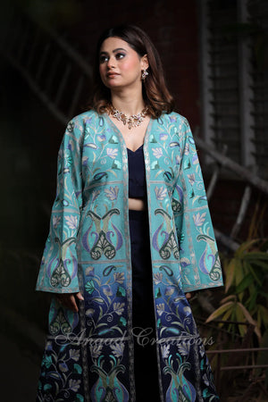 #OmbreBlue&Green Woman wearing a teal embroidered jacket over a black outfit with floral patterns.