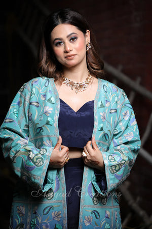 #OmbreBlue&Green Woman wearing a teal embroidered jacket with a dark background