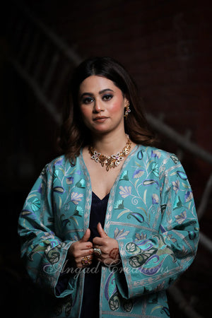 #OmbreBlue&Green Woman wearing a teal embroidered jacket with a dark background