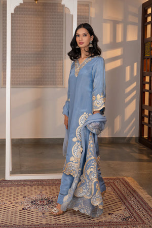 Side profile of sky blue tissue kurta showing scalloped hem border with large paisley zari embroidery and fitted straight pants.