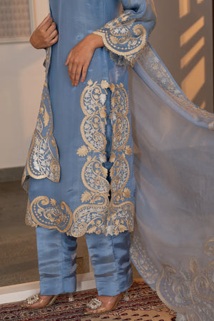 Detail shot of lower kurta hem and straight pants showing dense scalloped paisley zari border in gold and silver on sky blue tissue.