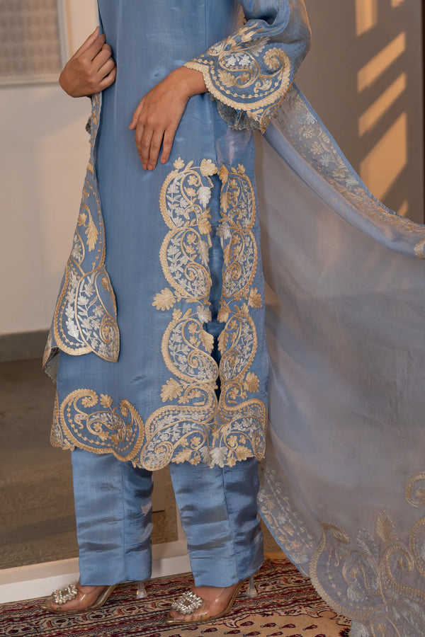 Detail shot of lower kurta hem and straight pants showing dense scalloped paisley zari border in gold and silver on sky blue tissue.