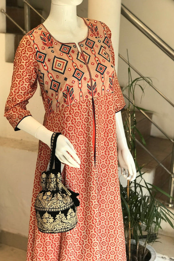 #black Mannequin wearing a red patterned dress holding a black and gold handbag indoors.