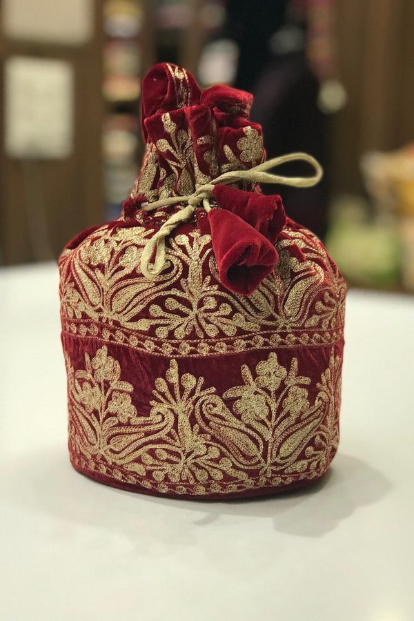 #red Decorative red and gold fabric pouch with floral elements on a white surface.