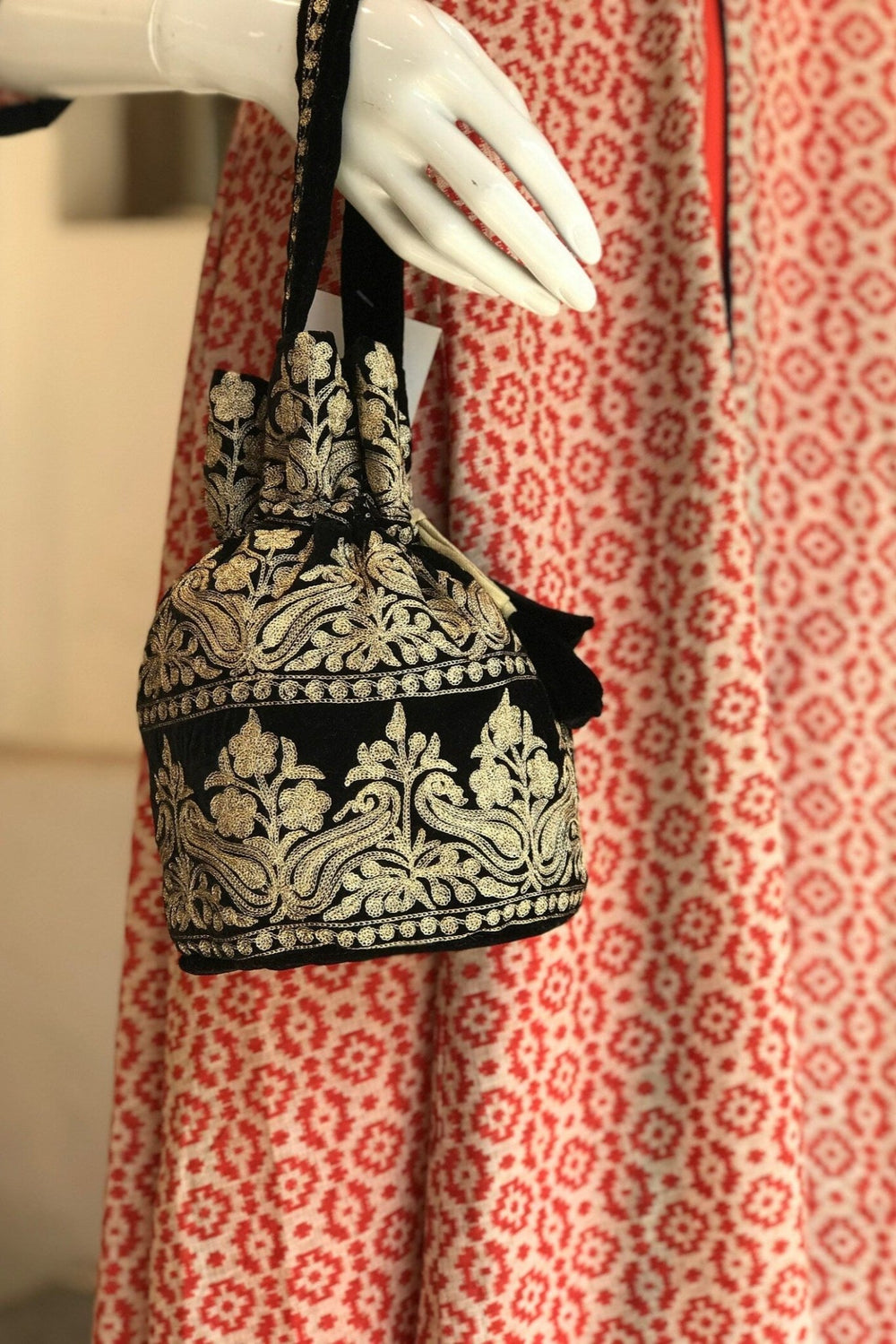 #Black Black embroidered handbag held by a mannequin against a red and white patterned fabric background