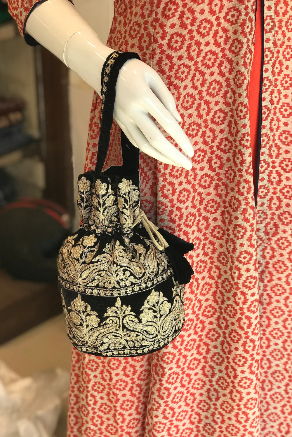 #Black Black embroidered handbag held by a mannequin against a red and white patterned fabric background