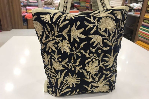 Decorative tote with gold floral pattern on a black background, placed on a white surface.